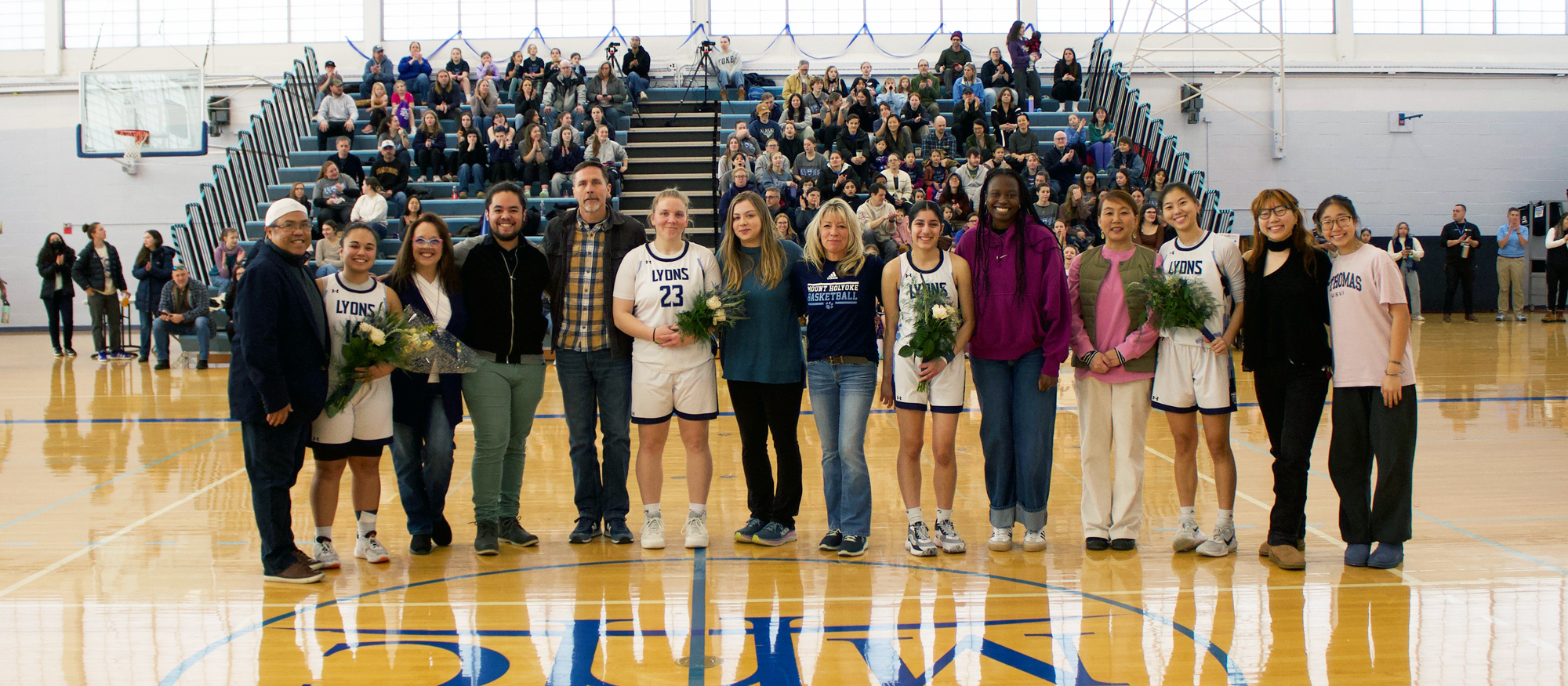 Members of Mount Holyoke basketball's Class of 2025 pose with family and supporters before their Senior Day game against Emerson on Feb. 8, 2025. (Alex Dizes)